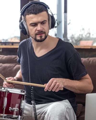 A young man with headphones learns to play the drum using online lessons.
