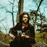 instructor, lennox with his guitar in the woods