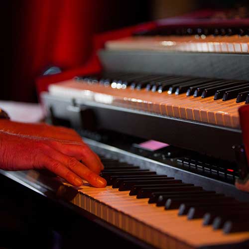 A pianists hands on the bottom keyboard of a stack of three electric pianos