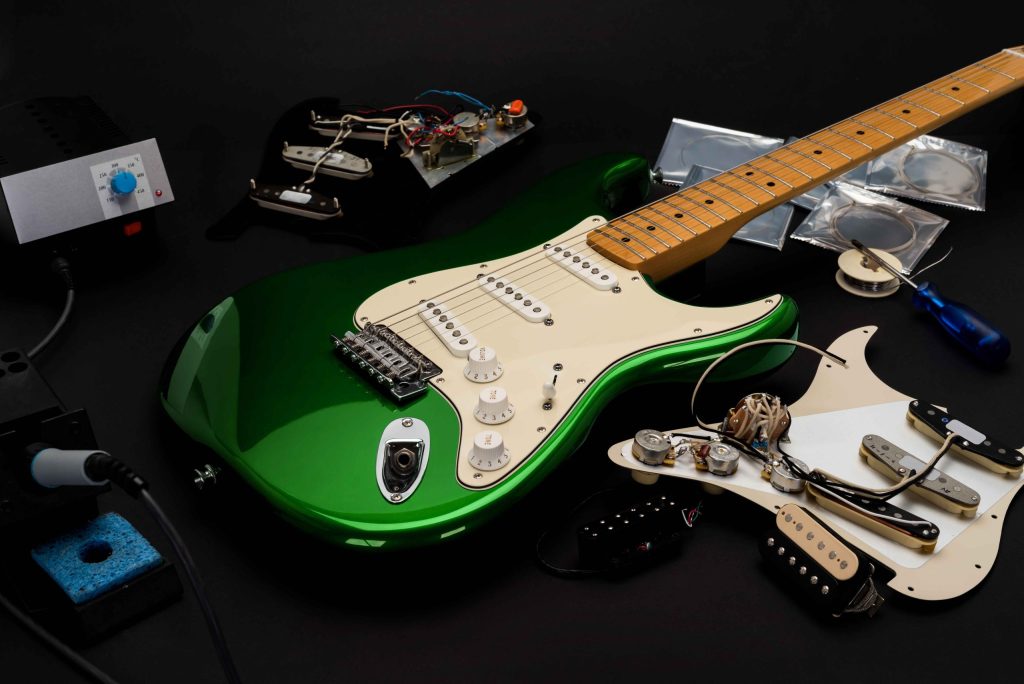 A metallic finished green guitar on a table with parts and accessories around it
