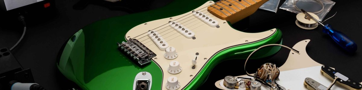 A metallic finished green guitar on a table with parts and accessories around it