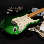 A metallic finished green guitar on a table with parts and accessories around it