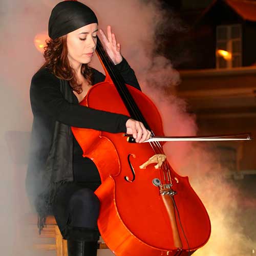 A woman in a bandana playing cello on stage with dry ice smoke effect around her