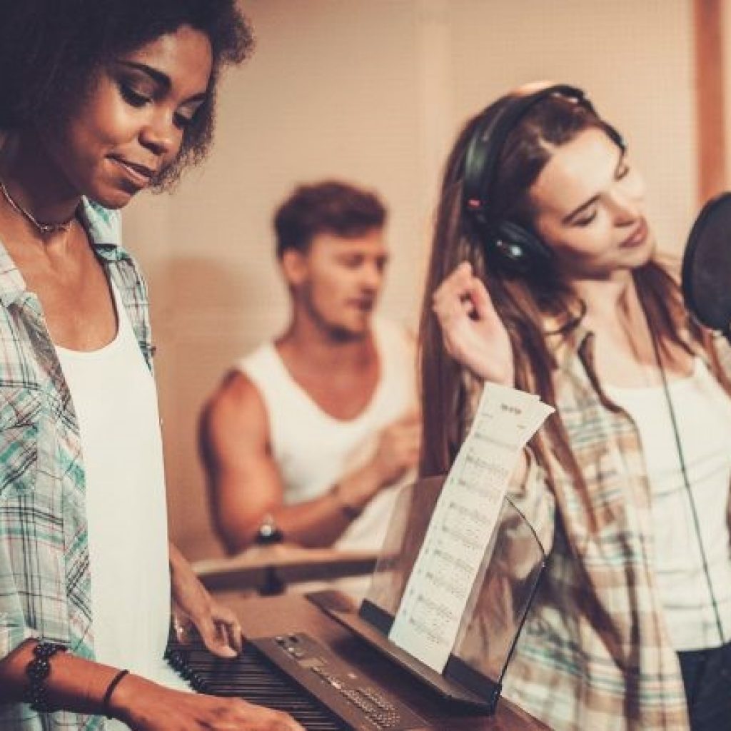 A singer, a drummer and a pianist performing in studio.