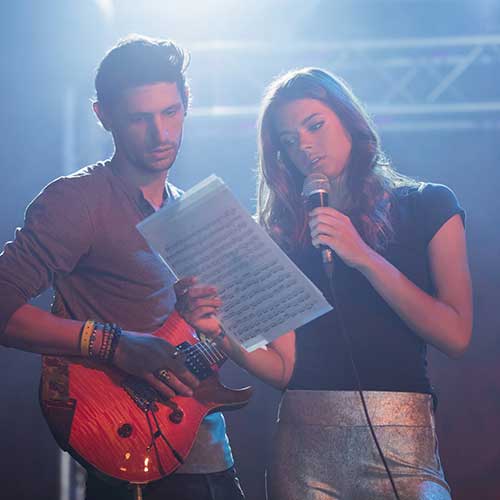 A singer and guitarist on stage, going over sheet music in sound check before a show