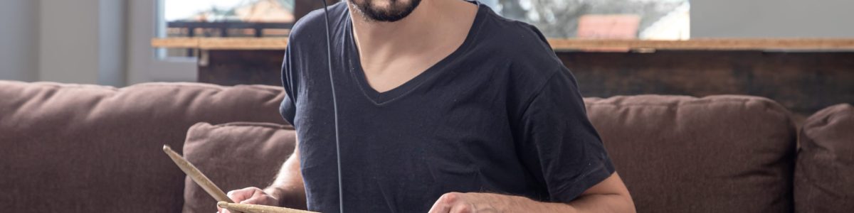 A young man with headphones learns to play the drum using online lessons.